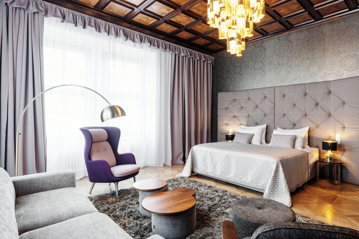 A modern bedroom with a tufted headboard, a large bed, a sofa, and a chair.