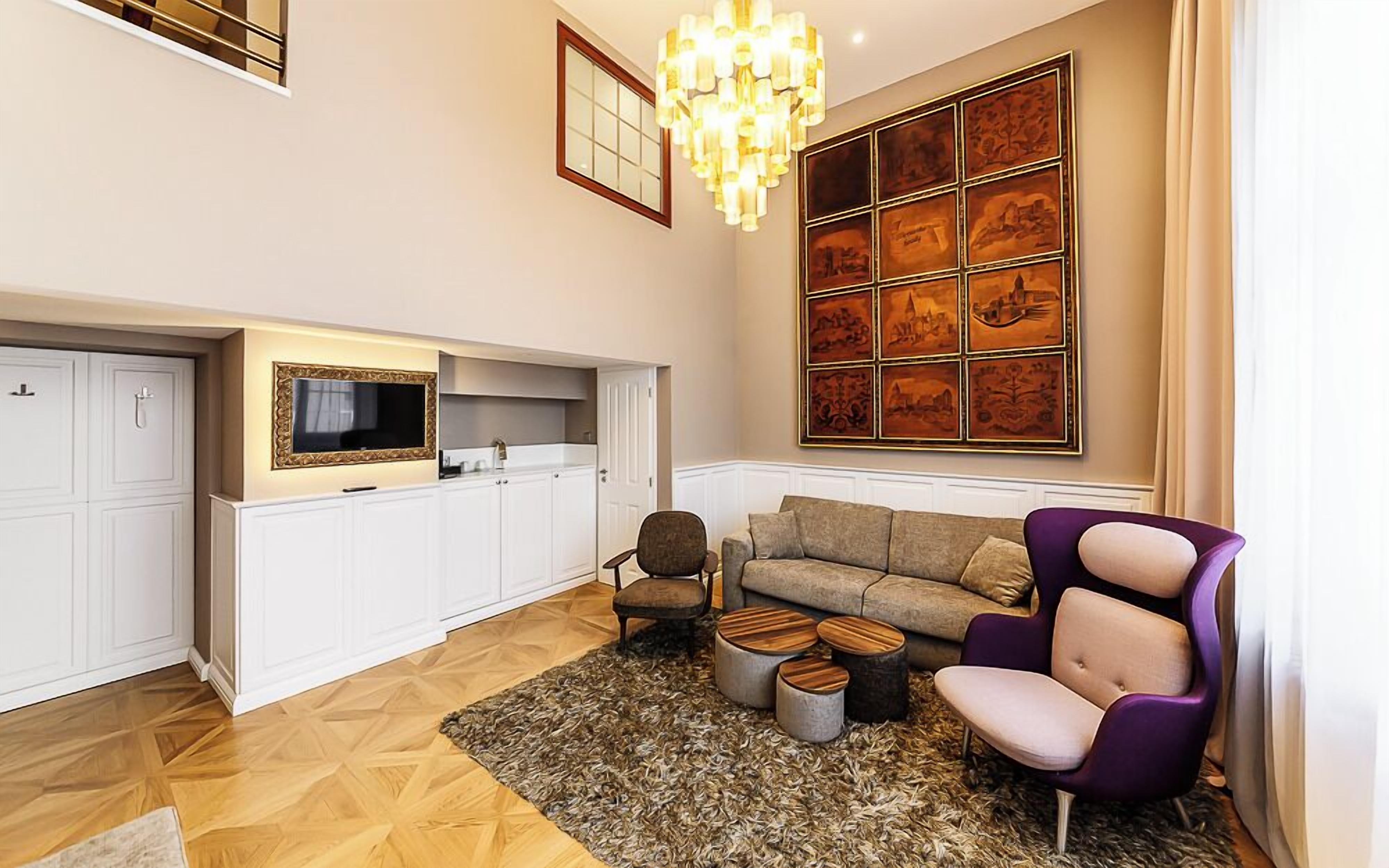 A spacious living room with a sofa, armchairs, a TV, and a large artwork on the wall.