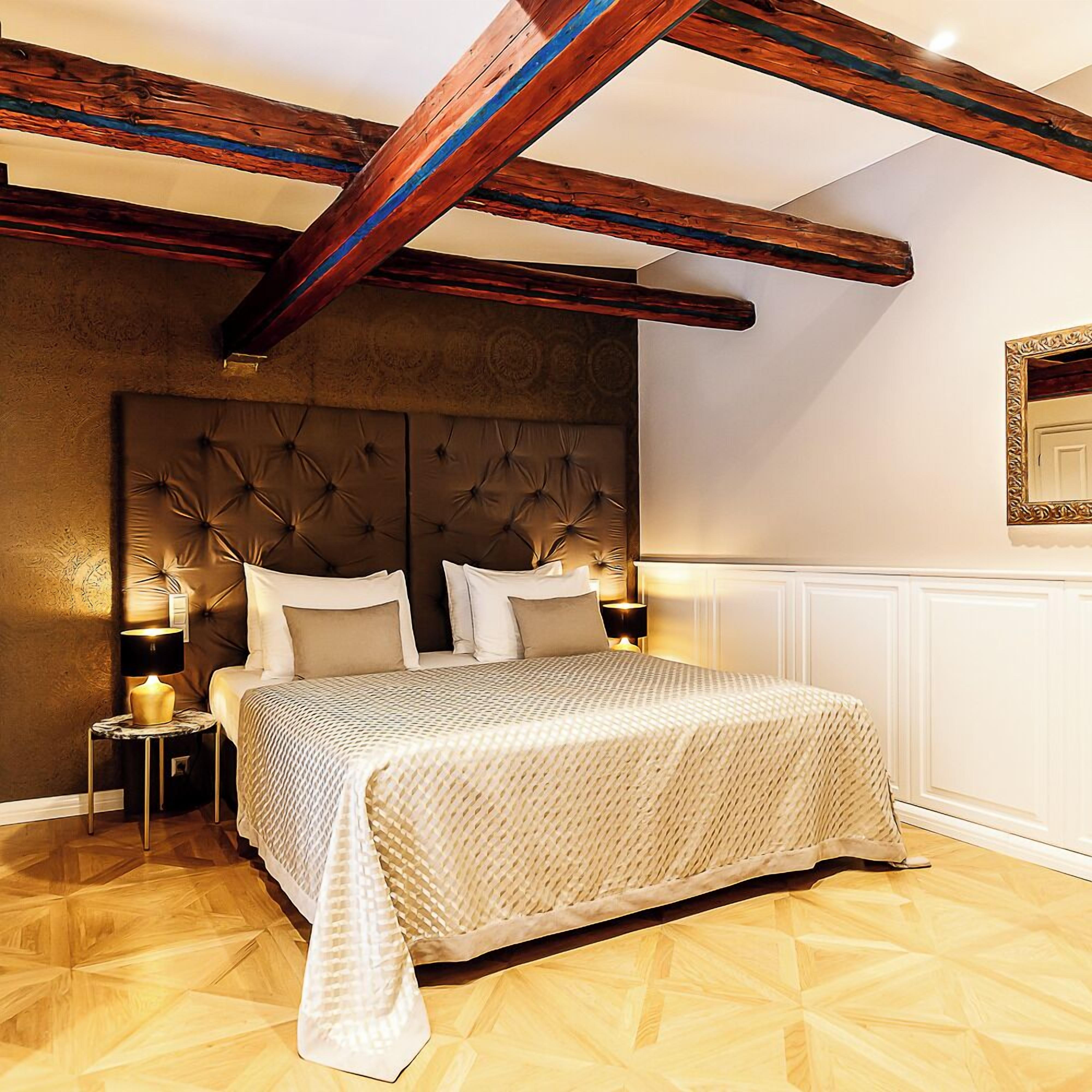 Ein Schlafzimmer mit einem großen Bett, Holzbalken, einem gemusterten Kopfteil und einem Nachttisch mit Lampe.