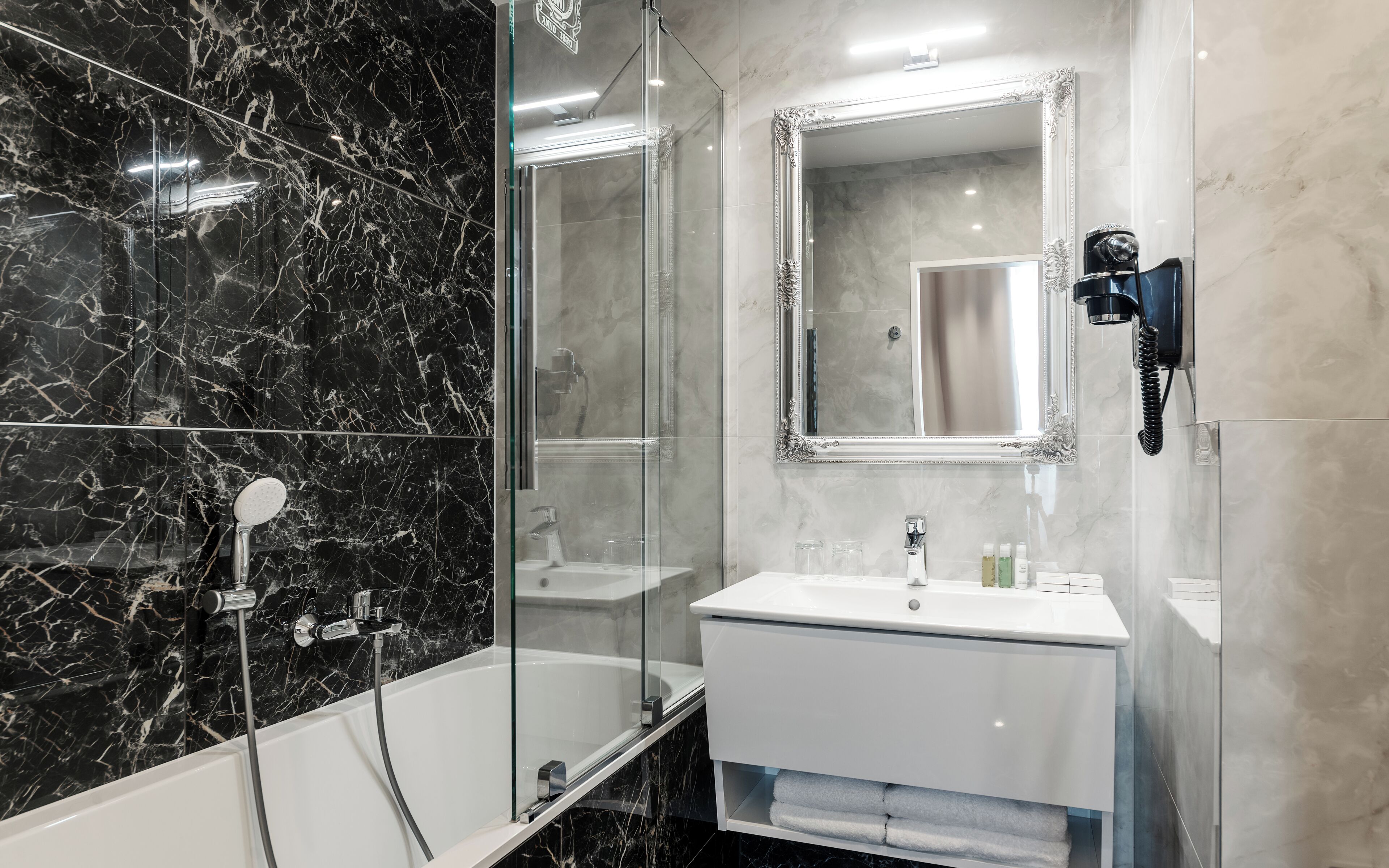 Un baño moderno con ducha envuelta en vidrio, un lavabo blanco con un espejo encima y un secador de pelo montado en la pared.