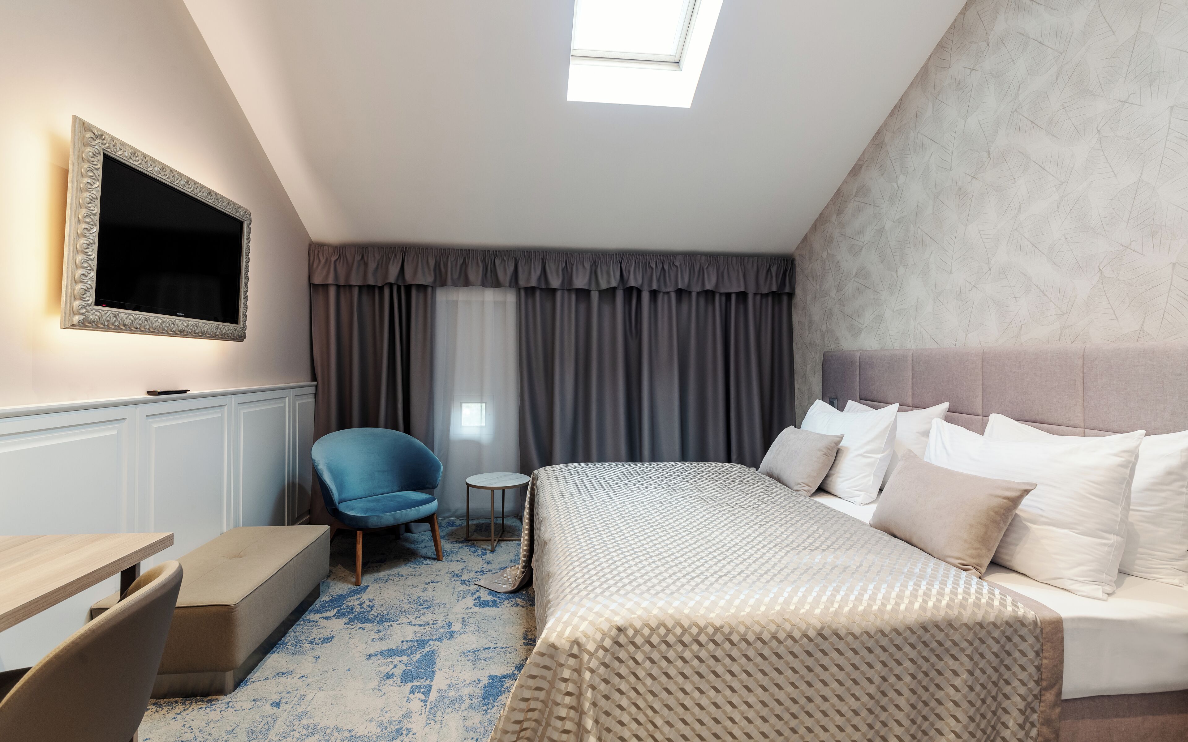 A modern hotel room with a large bed, a desk, a chair, and a television.