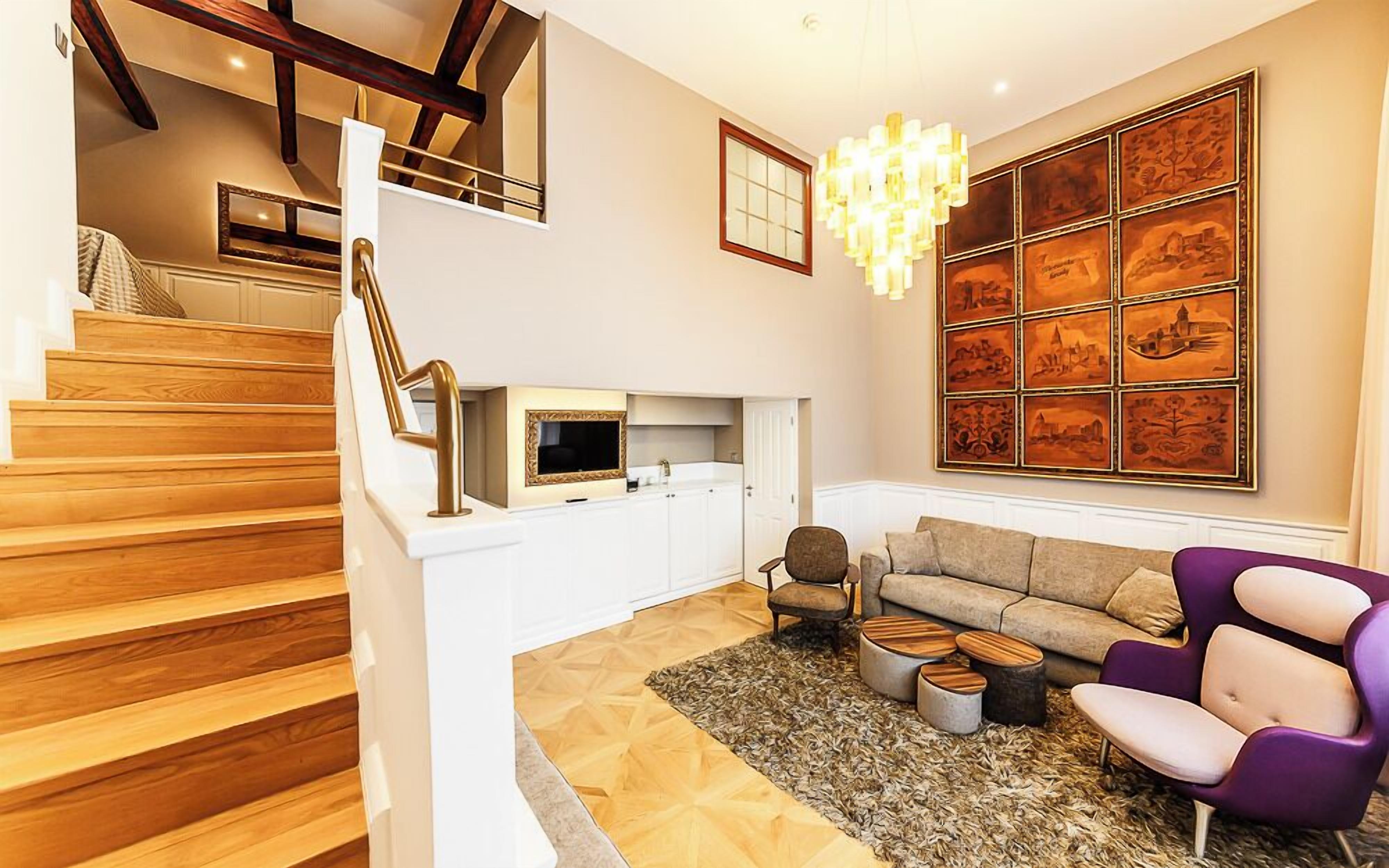 Ein modernes Wohnzimmer mit Treppe, einer Chandelüster und einer großen Wand mit gerahmten Kunstwerken.
