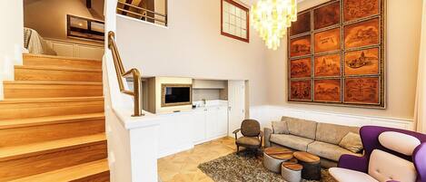 Ein modernes Wohnzimmer mit Treppe, einer Chandelüster und einer großen Wand mit gerahmten Kunstwerken.