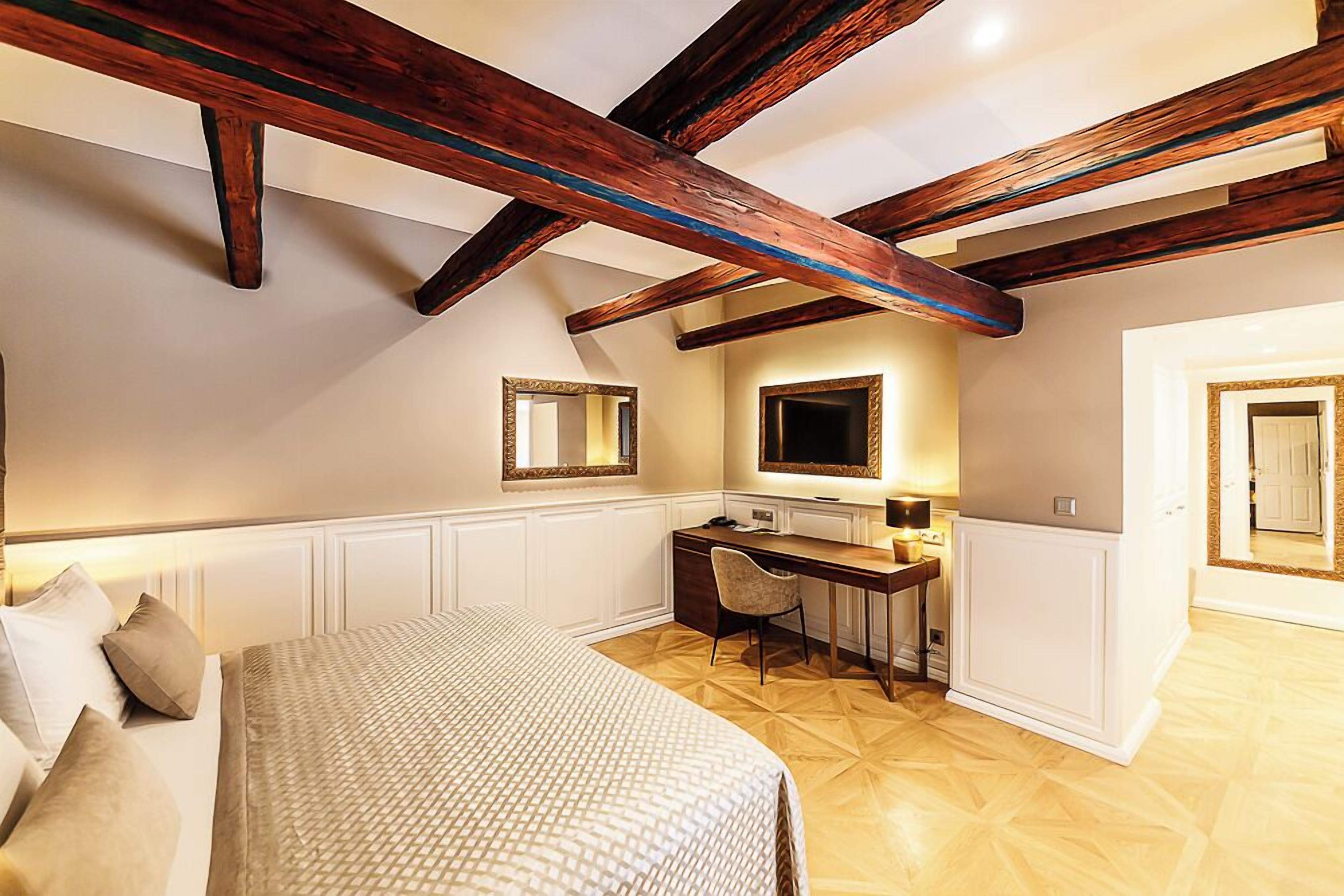 Un dormitorio con cama, escritorio y silla. Se observa un espejo en la pared y una puerta al fondo.
