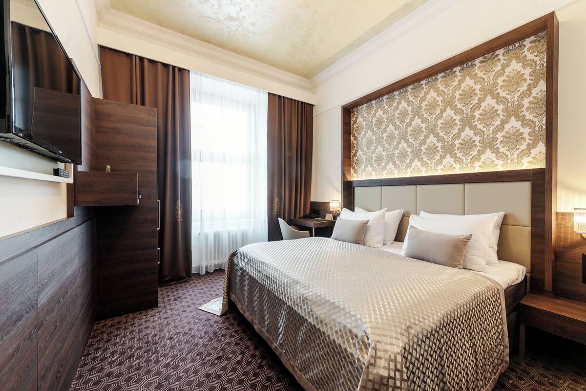 A hotel room with a large bed, a desk, a chair, a television, and a patterned headboard.