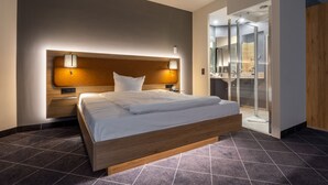 Una habitación de hotel moderna con una cama grande, un cabecero de madera y una cabina de ducha de vidrio.