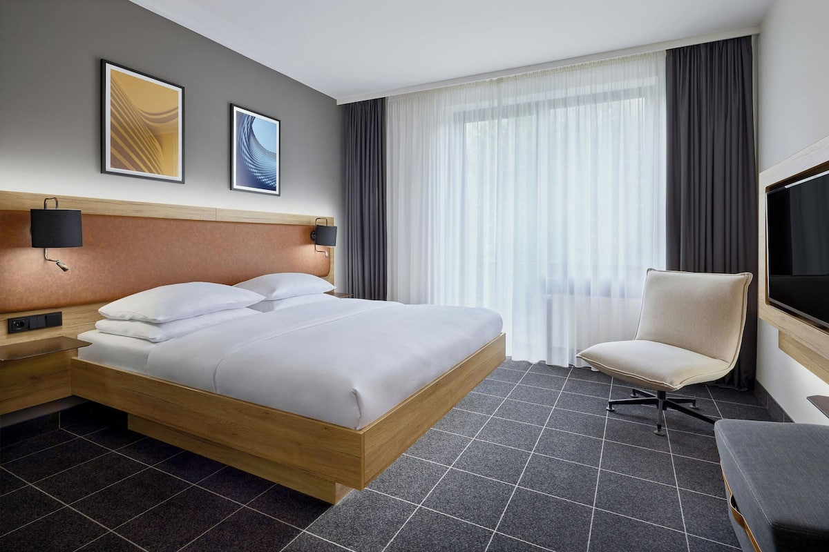 Une chambre d’hôtel avec un lit en bois, un bureau, une chaise, une télévision et deux tableaux encadrés au mur.