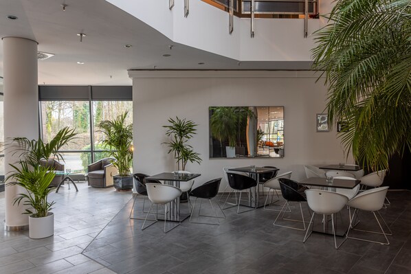Un espace intérieur moderne doté d’un coin repas avec une table et des chaises en verre, entouré de plantes en pot et de grandes fenêtres.