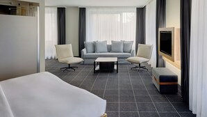 Una habitación de hotel moderna con una cama, dos sillones, un sofá, una mesita de centro y un televisor.
