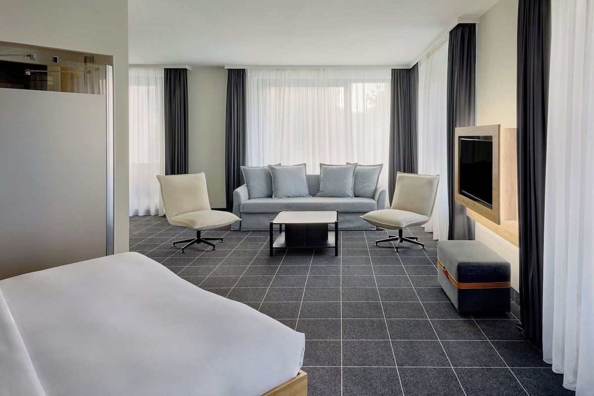 Une chambre d’hôtel moderne équipée d’un lit, de deux fauteuils, d’un canapé, d’une table basse et d’un téléviseur.