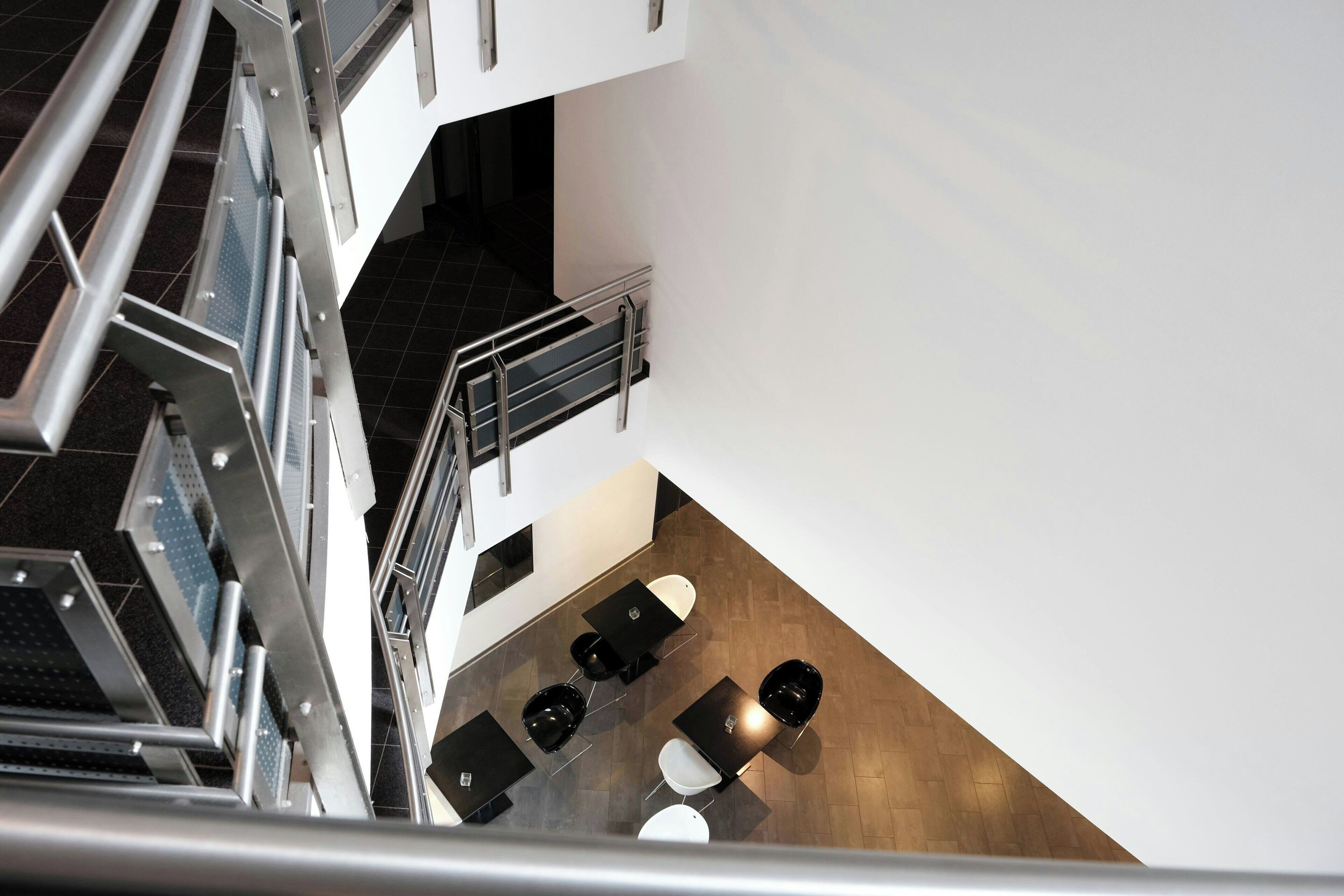 Un intérieur moderne avec un escalier, des rampes en métal et un espace salon comprenant des tables et des chaises.