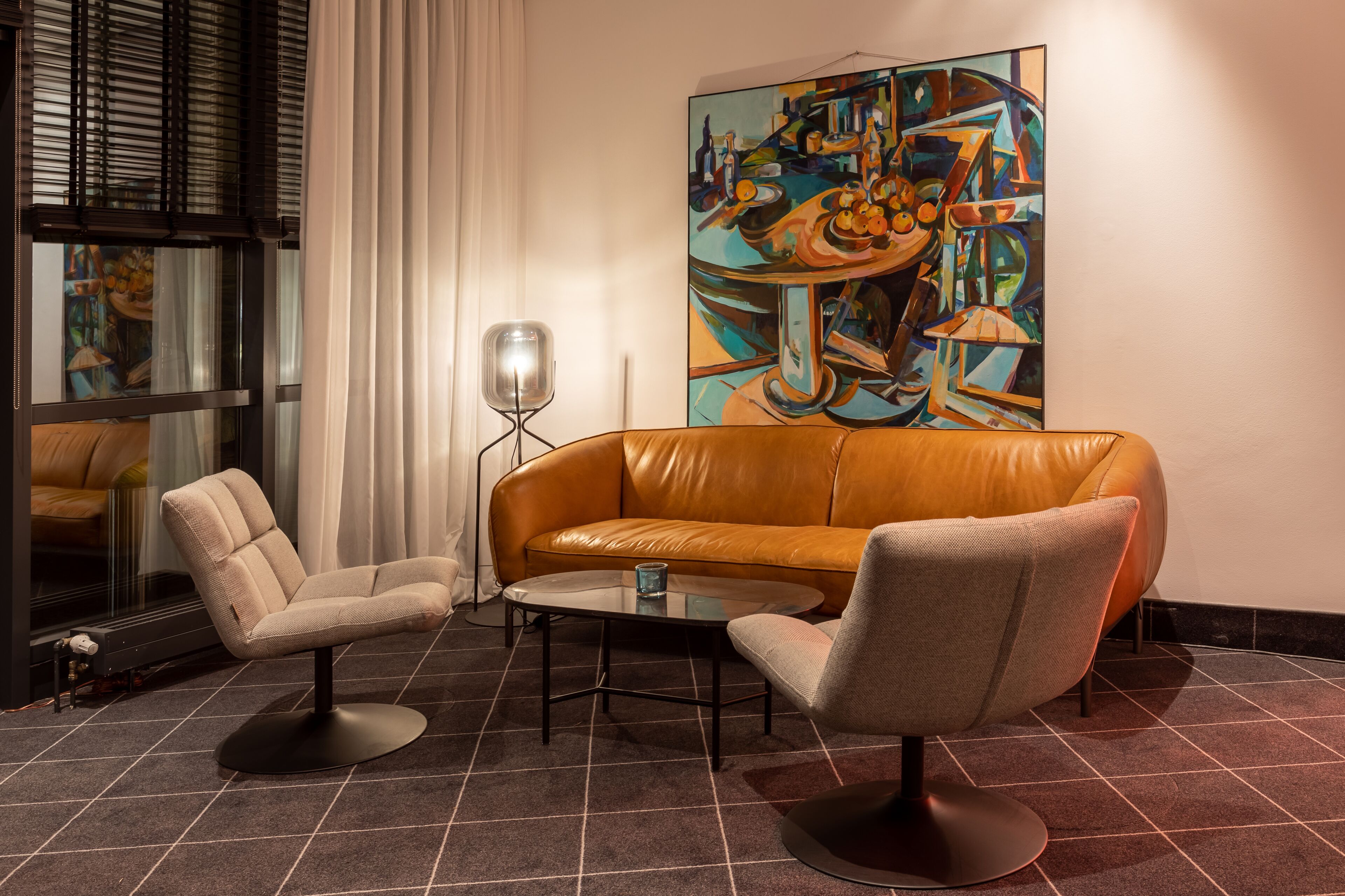 A modern living room with a leather sofa, two armchairs, a glass coffee table, and a large abstract painting on the wall.