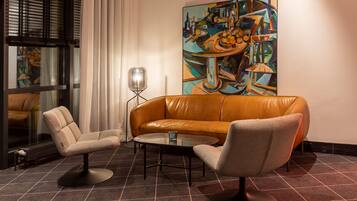 A modern living room with a leather sofa, two armchairs, a glass coffee table, and a large abstract painting on the wall.