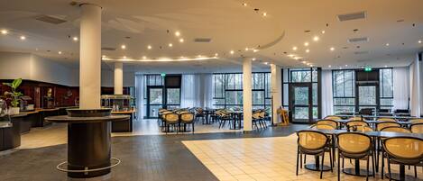 A spacious indoor area with multiple tables and chairs, large windows, and a central pillar.