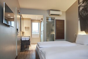 Una habitación de hotel moderna con una cama, un baño con espejo y un equipo de aire acondicionado.