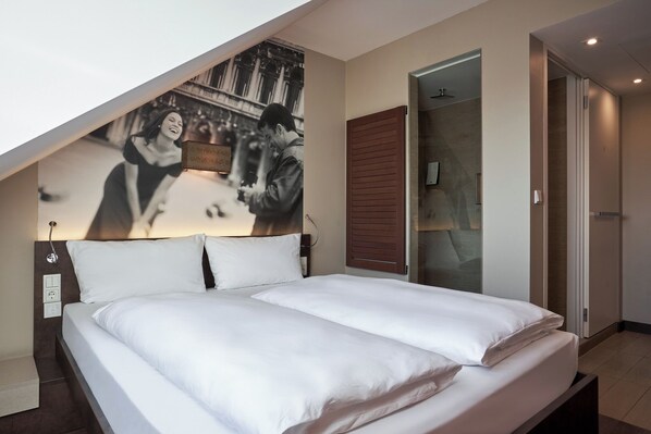 Een slaapkamer met een groot bed, een kunstwerk aan de muur, een houten deur en een glazen scheidingswand.