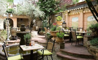 Un patio al aire libre con mesas y sillas de piedra, una fuente y plantas en macetas.