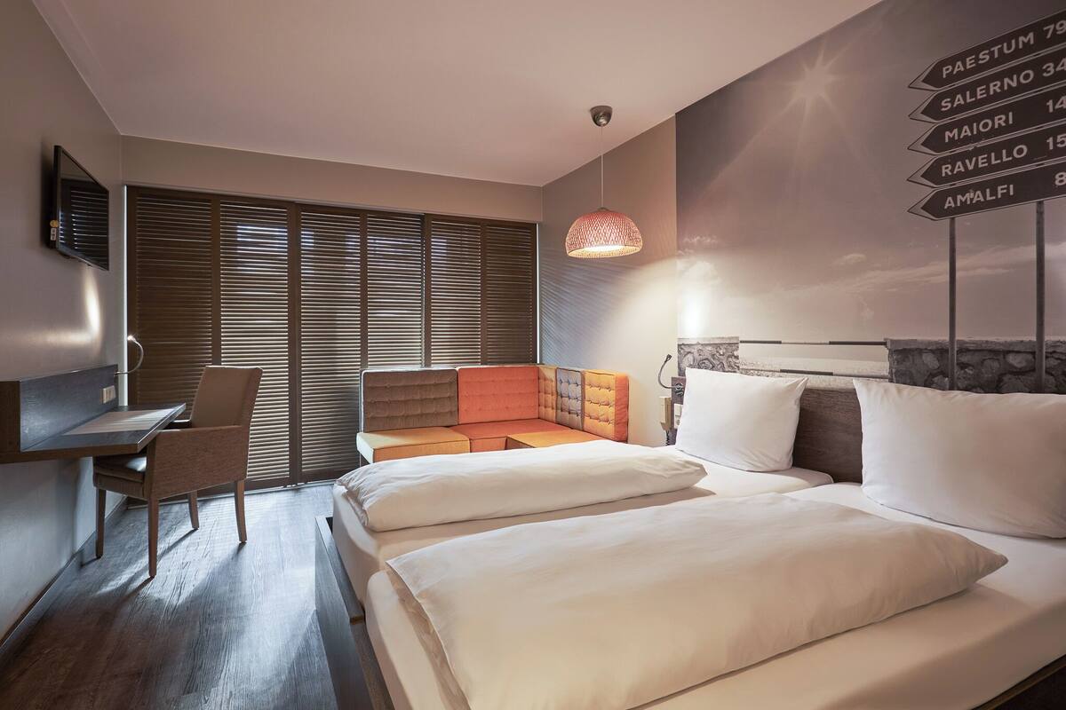 Habitación de hotel con cama, escritorio, silla, sofá y televisor montado en la pared.