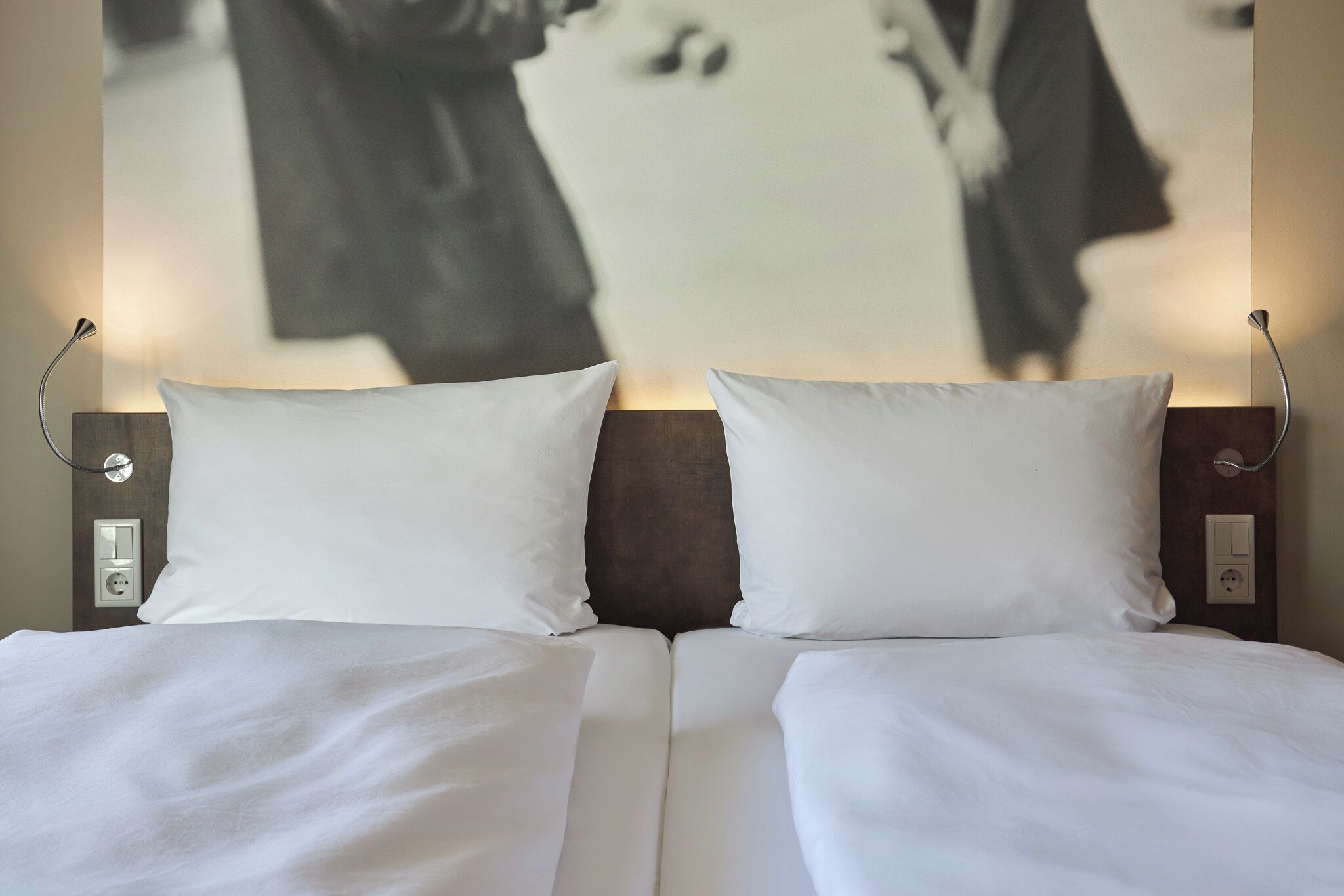 A double bed with white bedding, two bedside lamps, and a wall-mounted light fixture.