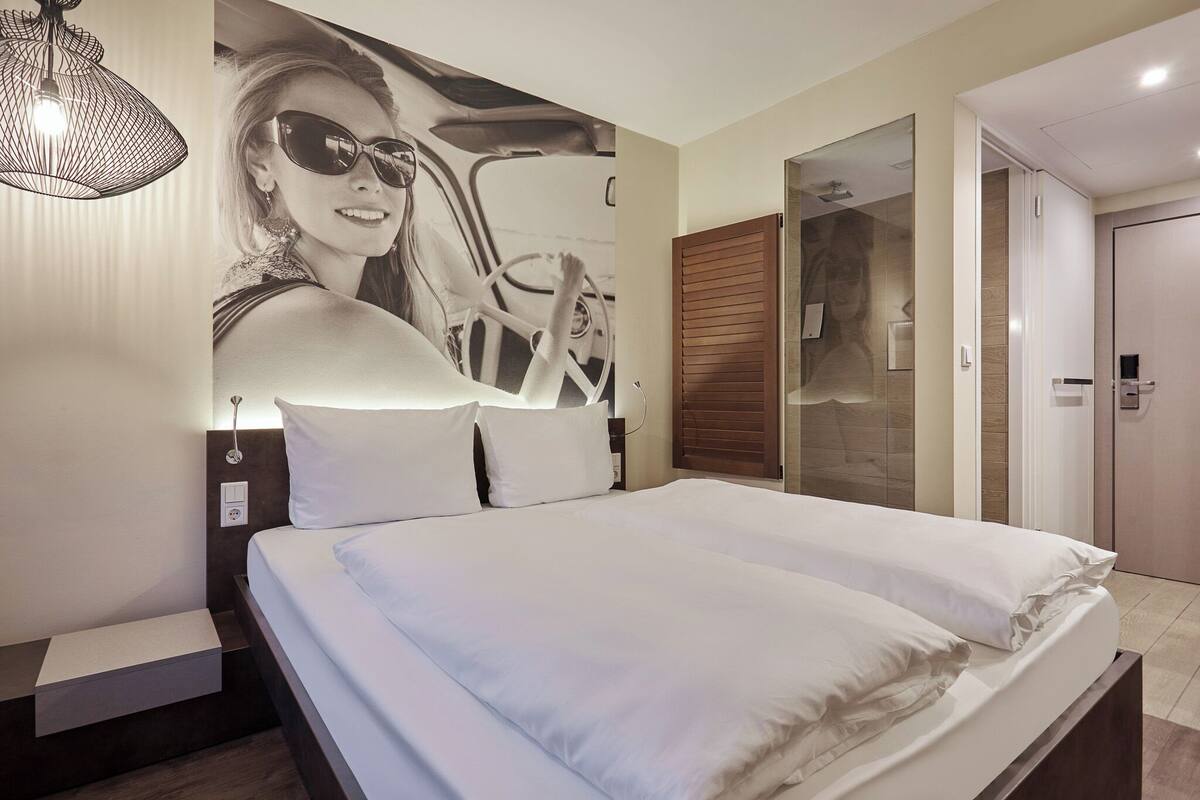 Habitación de hotel con cama, lámpara de pared, puerta y espejo.