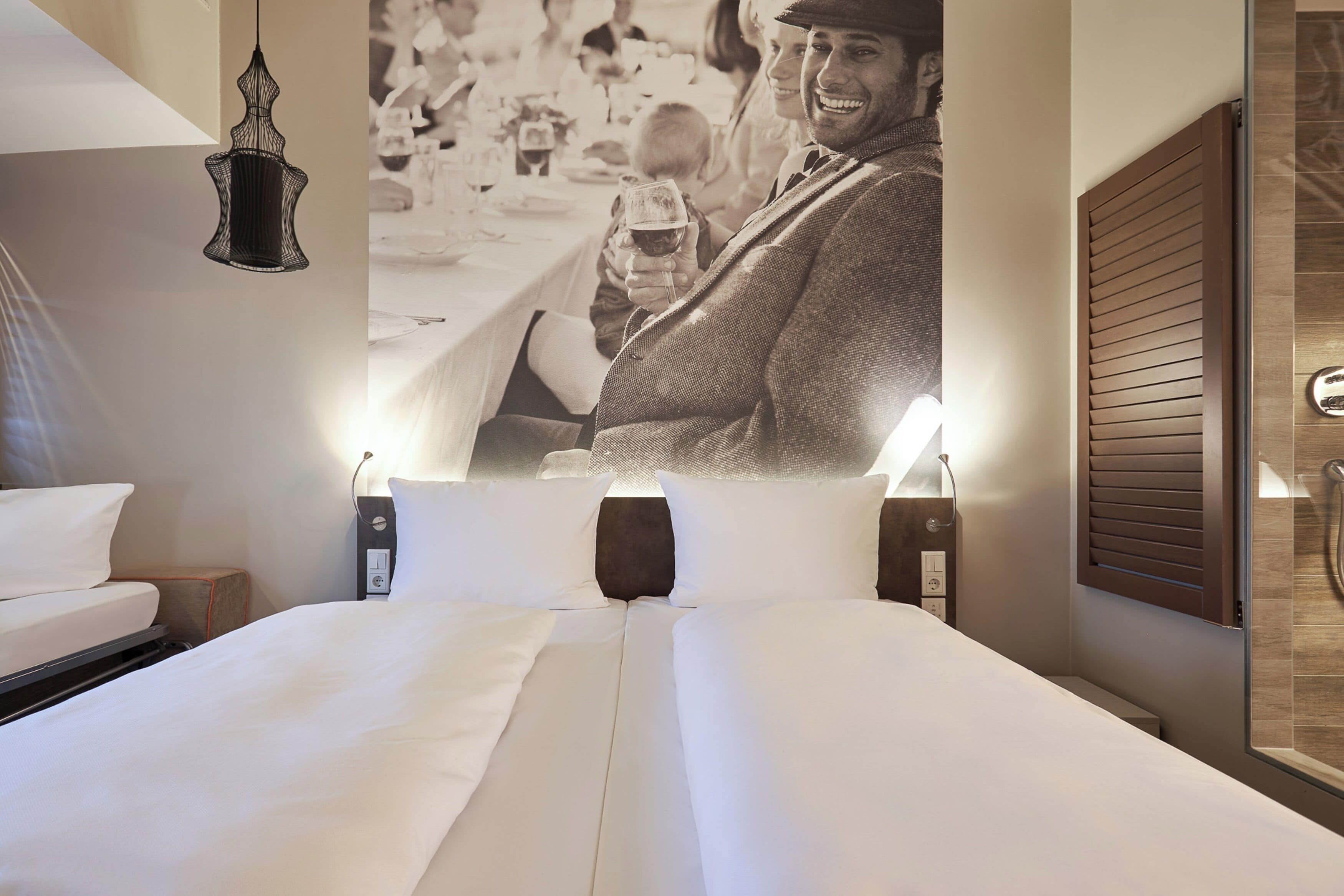 A hotel room with a large bed, bedside lamps, a wall-mounted light fixture, and a wooden panel on the wall.