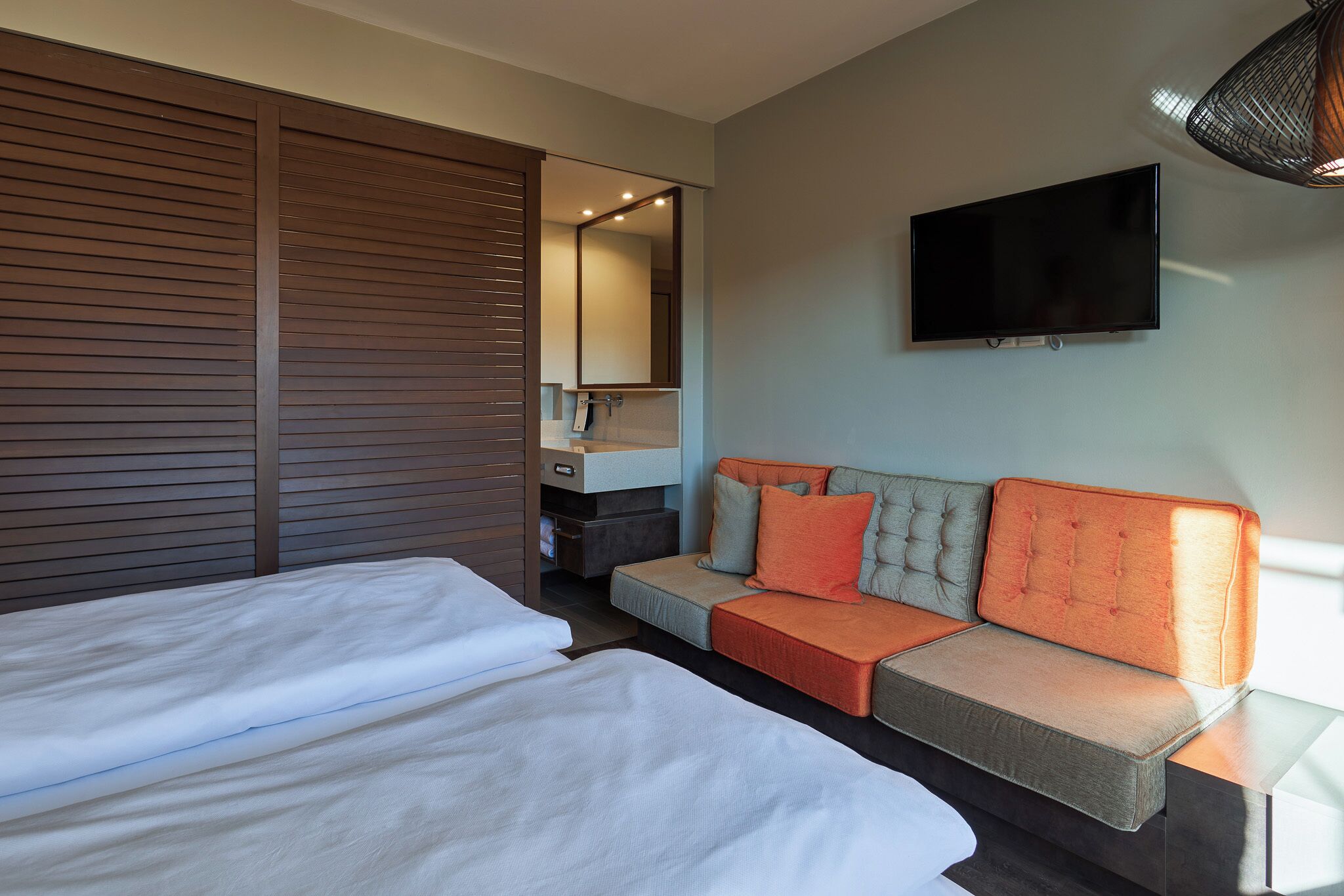 Une chambre d’hôtel avec deux lits, un canapé, une télévision et un miroir.