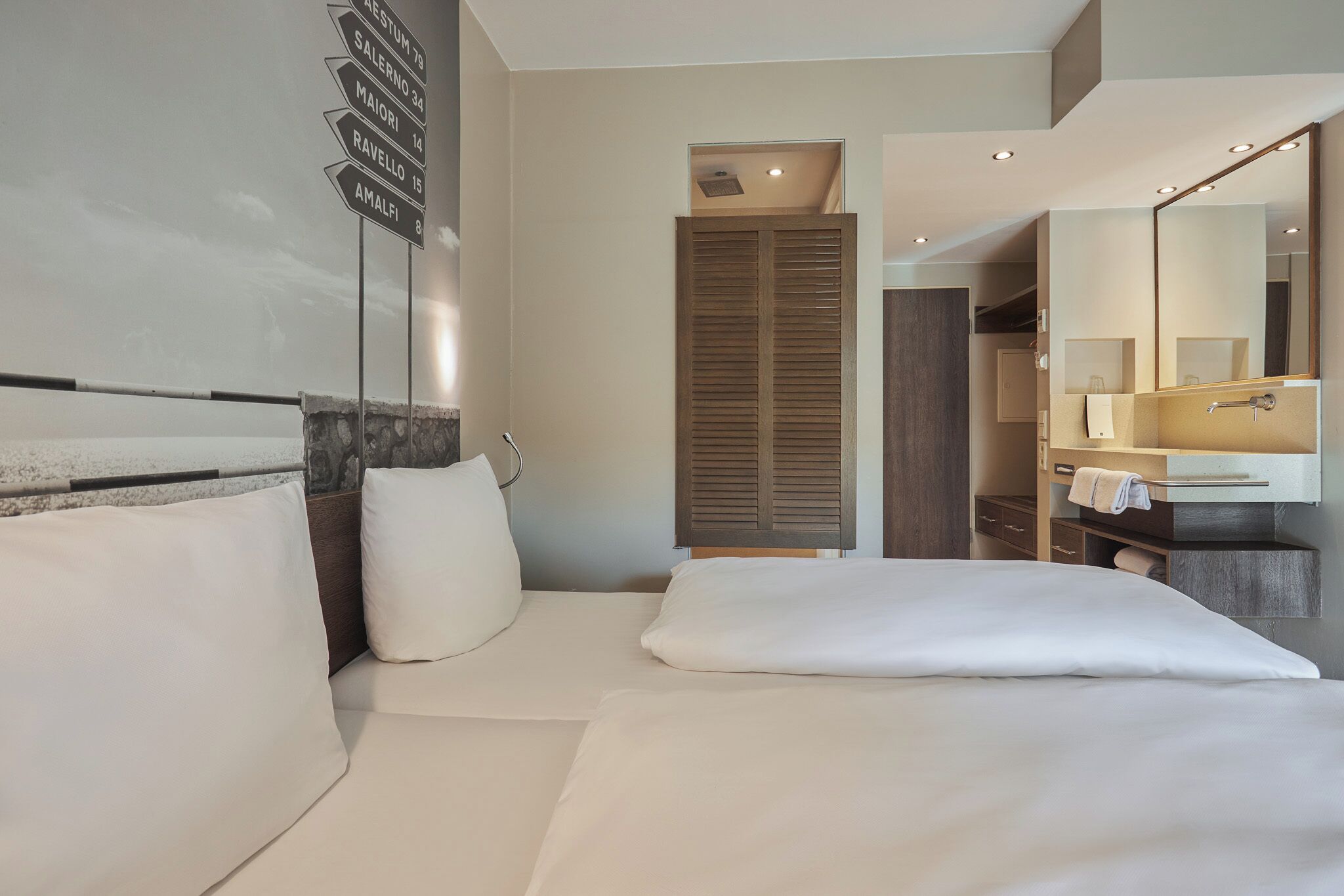 A hotel room with a bed, a mirror, a sink, and a wardrobe.