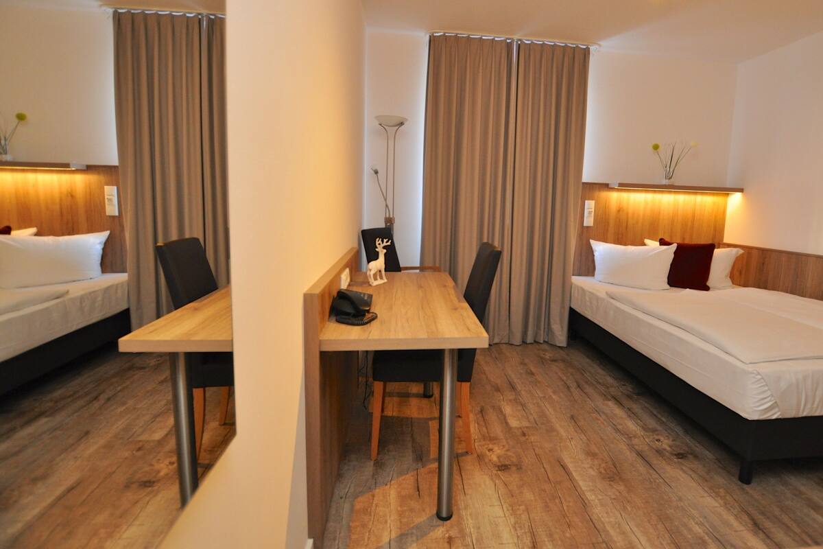 Habitación de hotel con dos camas, una mesa de madera y una lámpara.