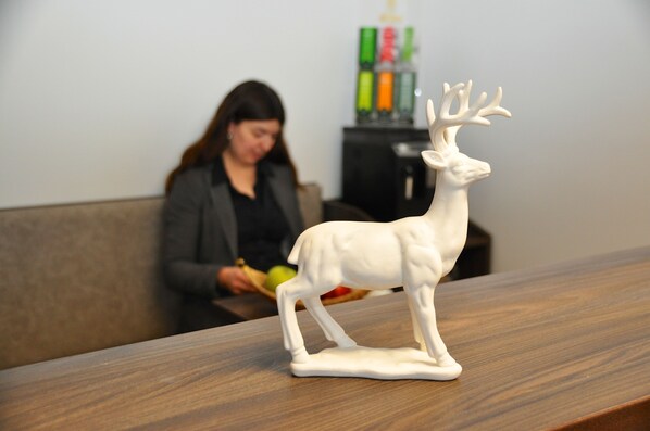 Una figurita de ciervo blanco sobre una mesa de madera en una habitación, con una persona al fondo.