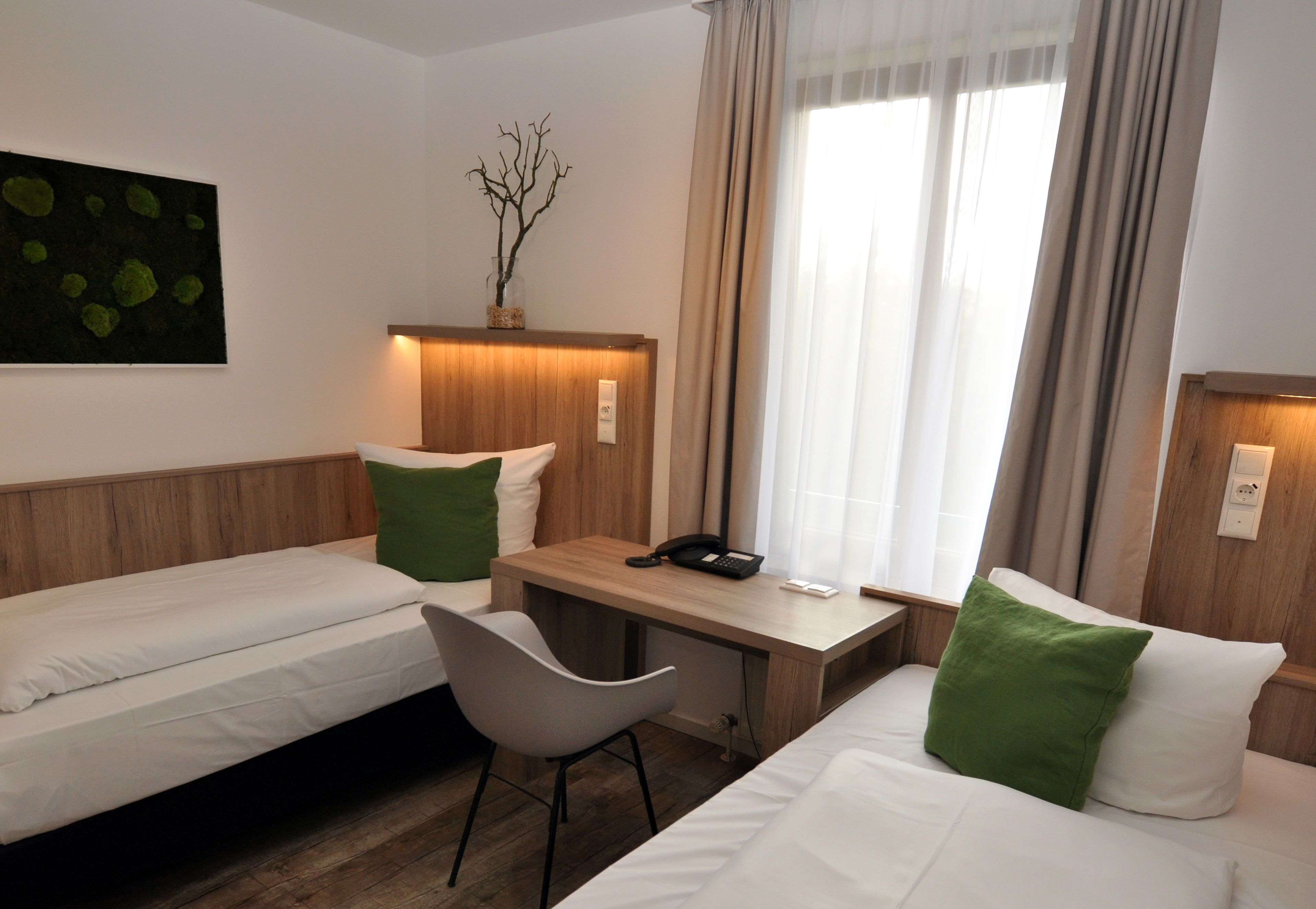 A hotel room with two single beds, a desk, a chair, and a small table.