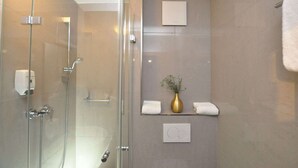Un baño moderno con cabina de ducha de vidrio, un perchero, una pequeña estantería con un jarrón y un interruptor de luz en la pared.