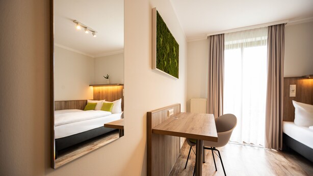 Una habitación de hotel moderna con cama, escritorio, silla y un espejo grande.