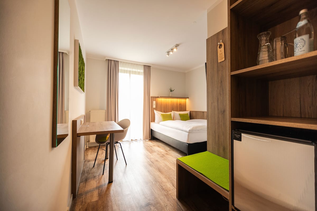 Una habitación de hotel con una cama, un escritorio, una silla, una mesita y una estantería.