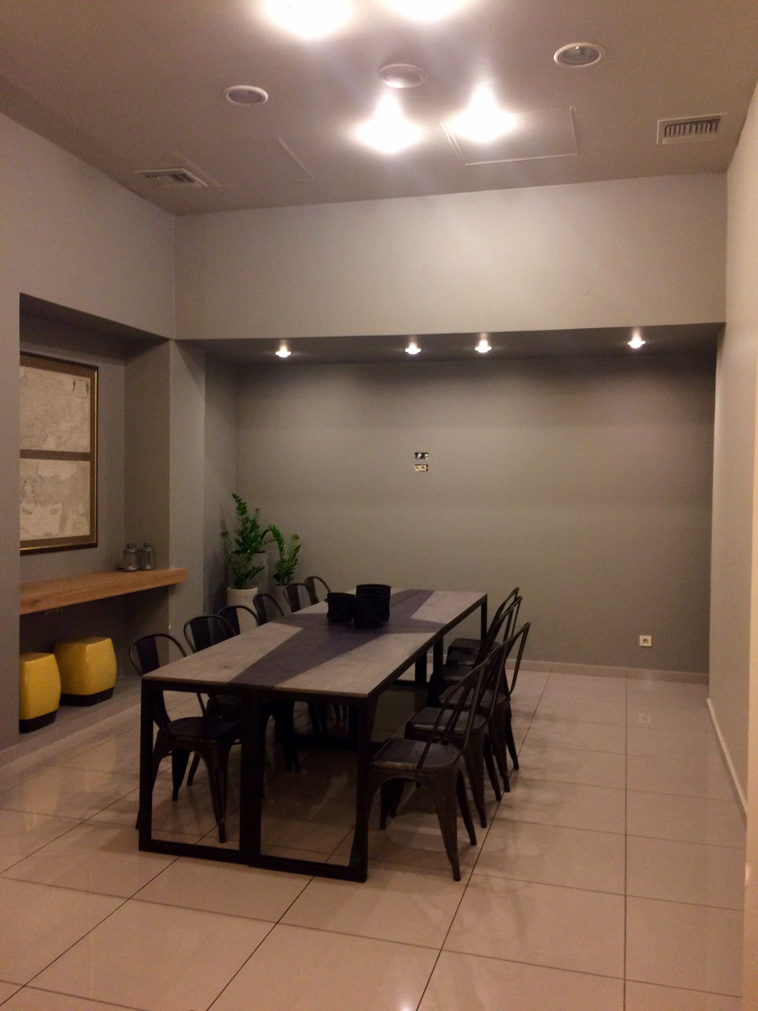 A conference room with a long table, chairs, a potted plant, and a shelf with items.