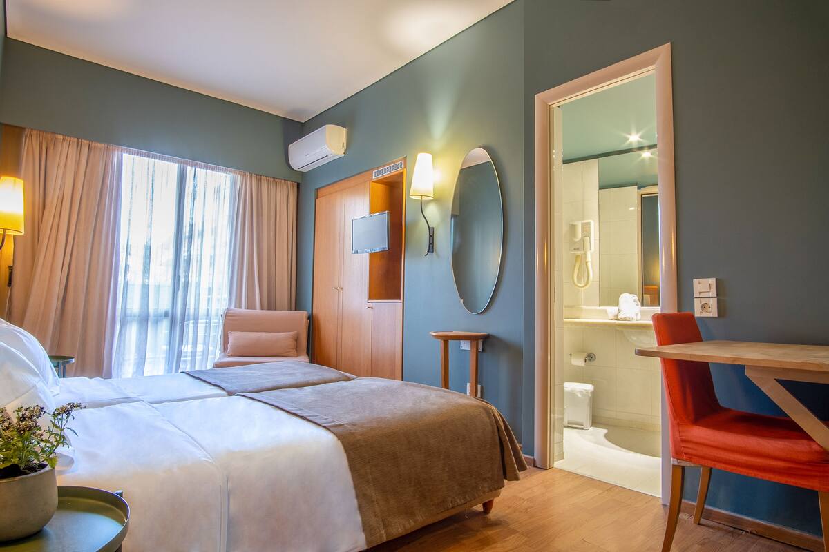 A hotel room with a bed, a desk, a chair, a mirror, a TV, and a bathroom.