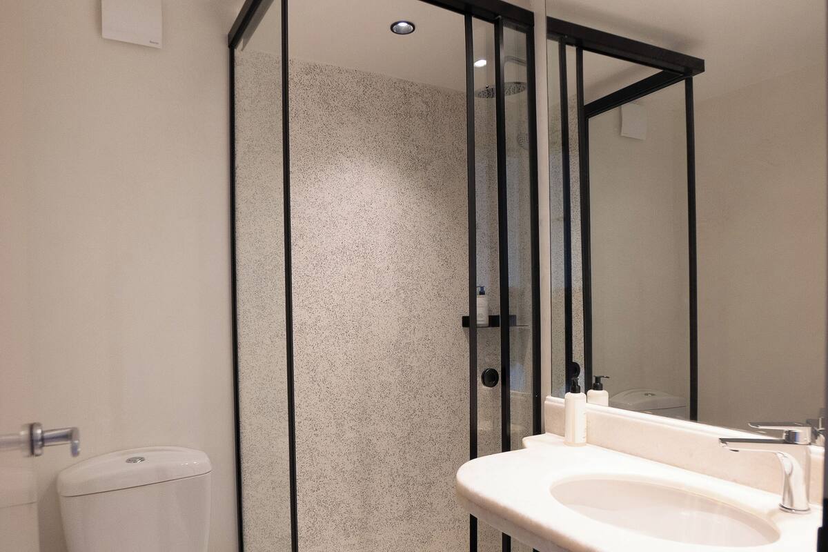 A modern bathroom with a glass-enclosed shower, a white toilet, and a vanity with a mirror.