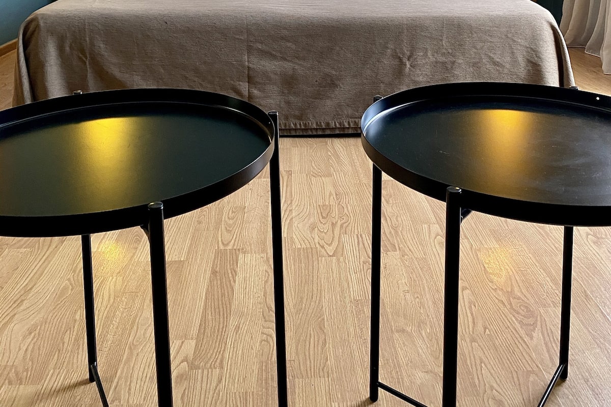 A hotel room with a double bed, two bedside tables, two lamps, and two small round tables.