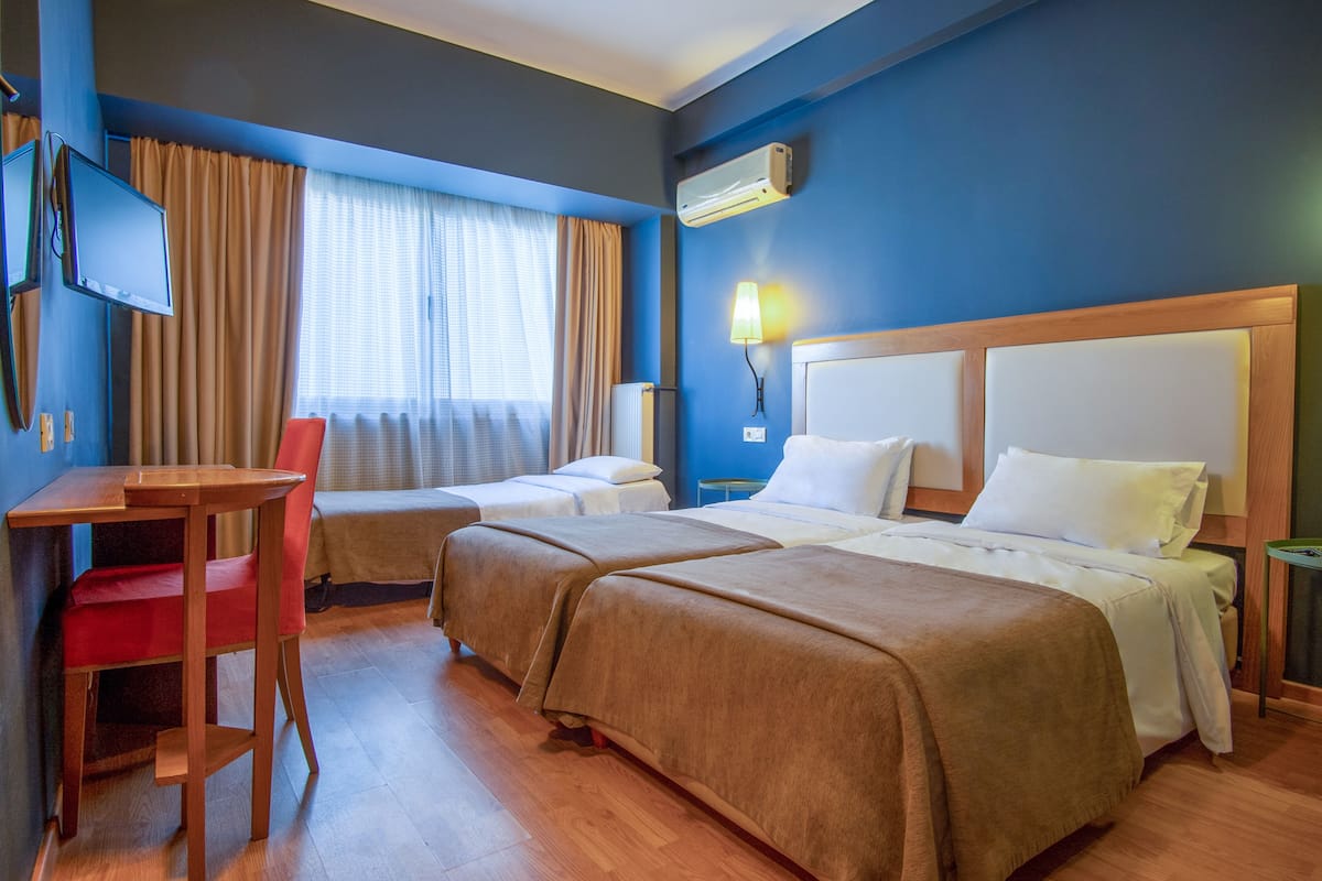 A hotel room with two beds, a desk, a chair, a TV, and a lamp.