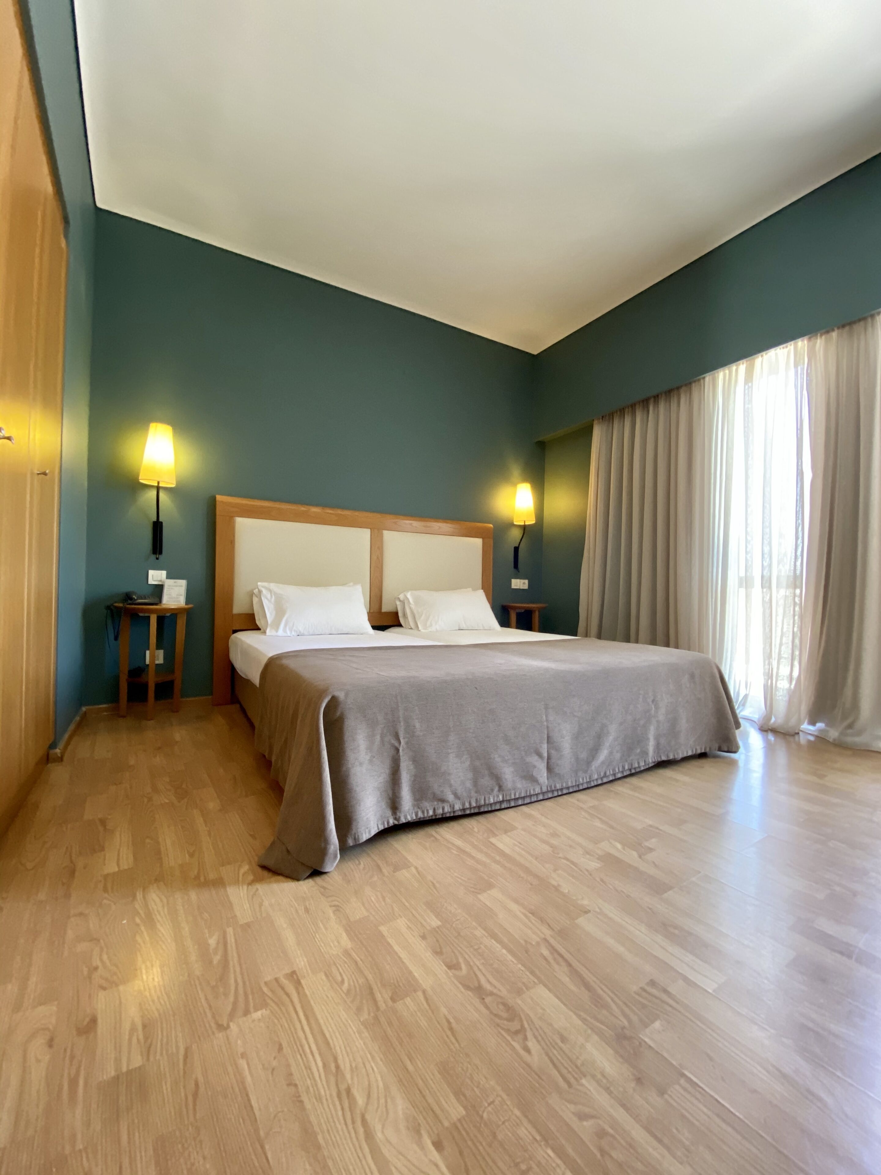 Una camera da letto con un letto grande, due comodini con lampade, un pavimento in legno e una finestra con tende.