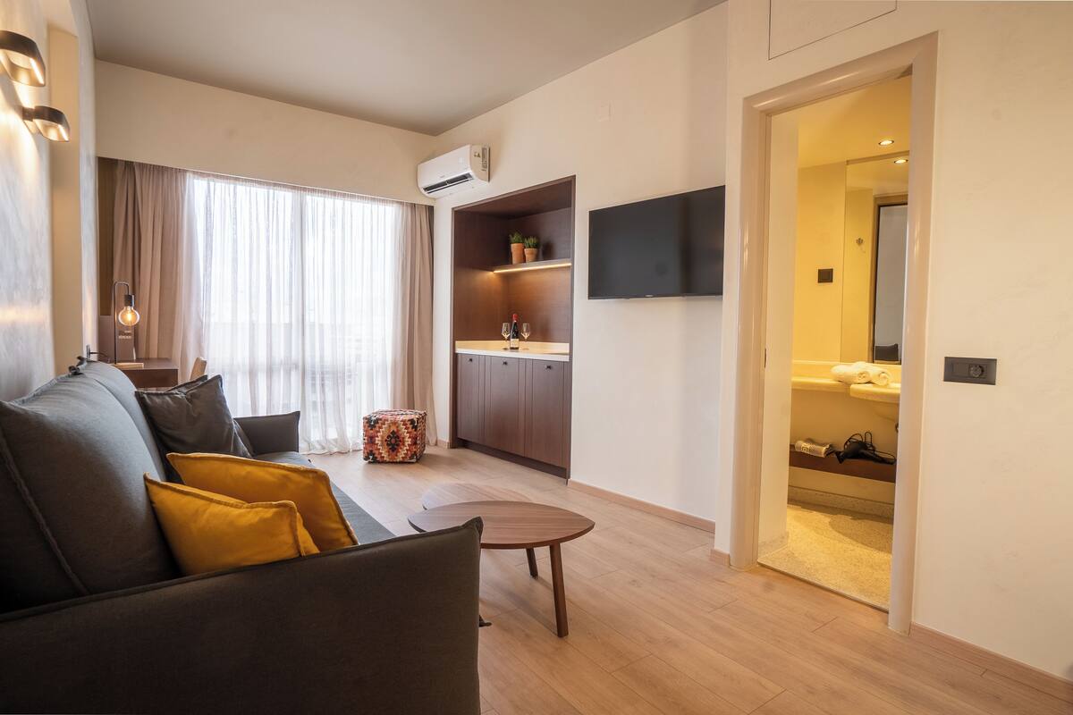 A modern living room with a sofa, a small round table, and a TV mounted on the wall.
