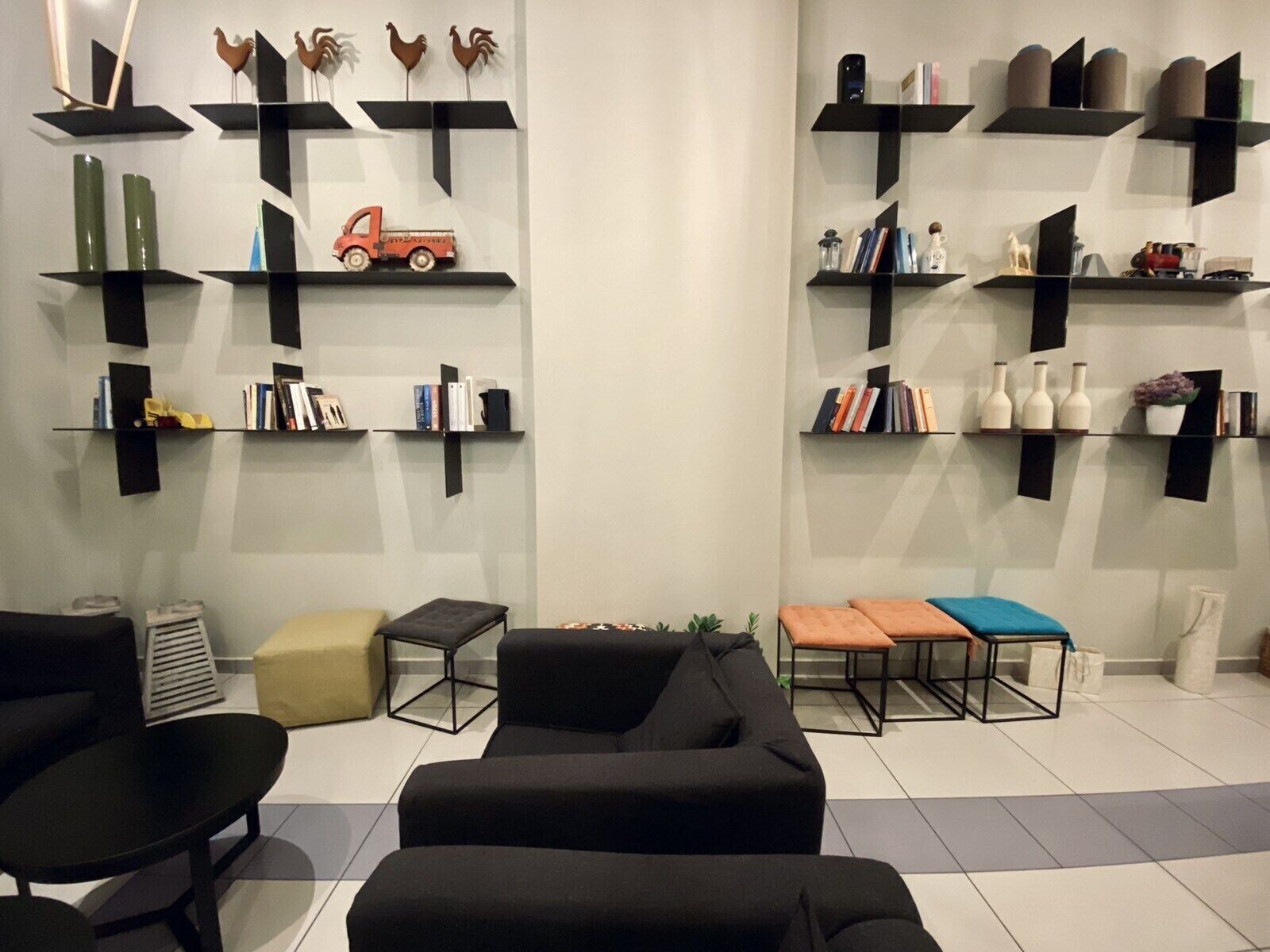 A modern living room with black sofas, a coffee table, and a bookshelf with decorative items.