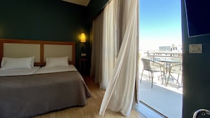 Habitación de hotel con cama, mesita de noche, lámpara y vistas al balcón exterior.