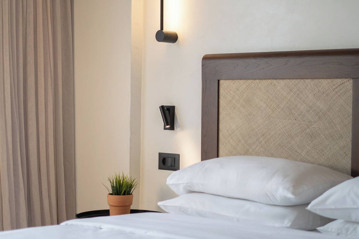 A neatly made bed with white linens, a wooden headboard, and a small potted plant on a bedside table.