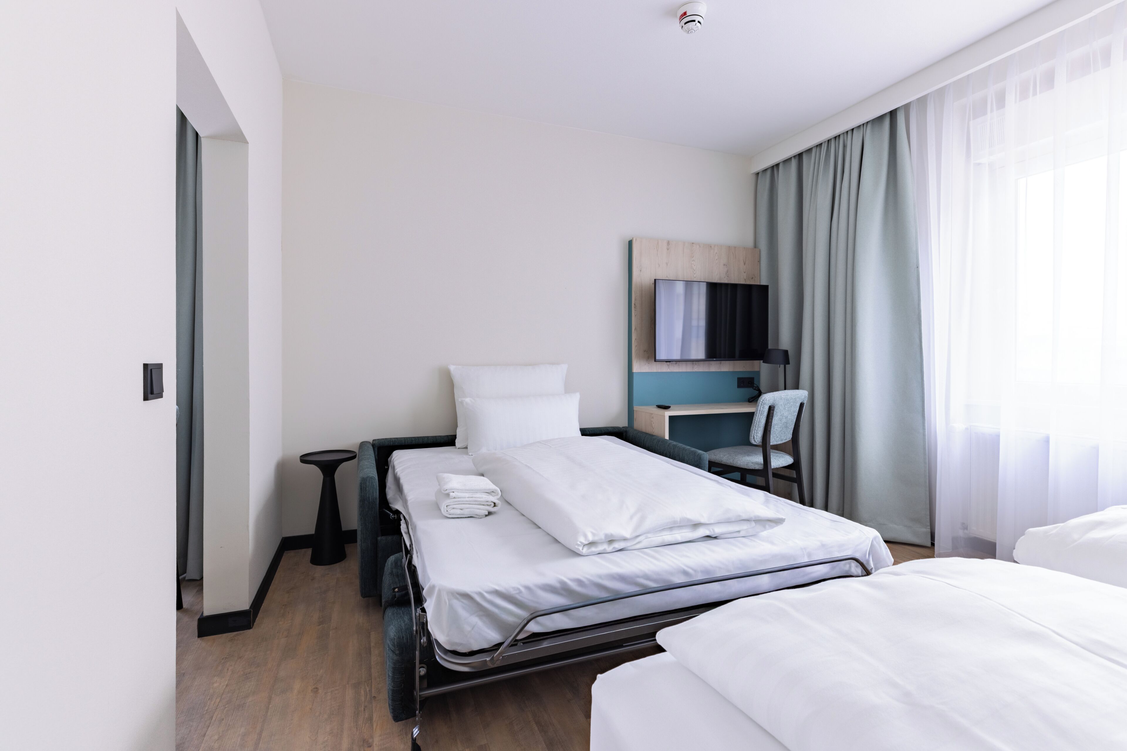 A hotel room with a bed, a desk, a chair, and a TV.