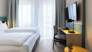 Una habitación de hotel con una cama, un escritorio con una computadora, una silla, un televisor y una ventana con cortinas.