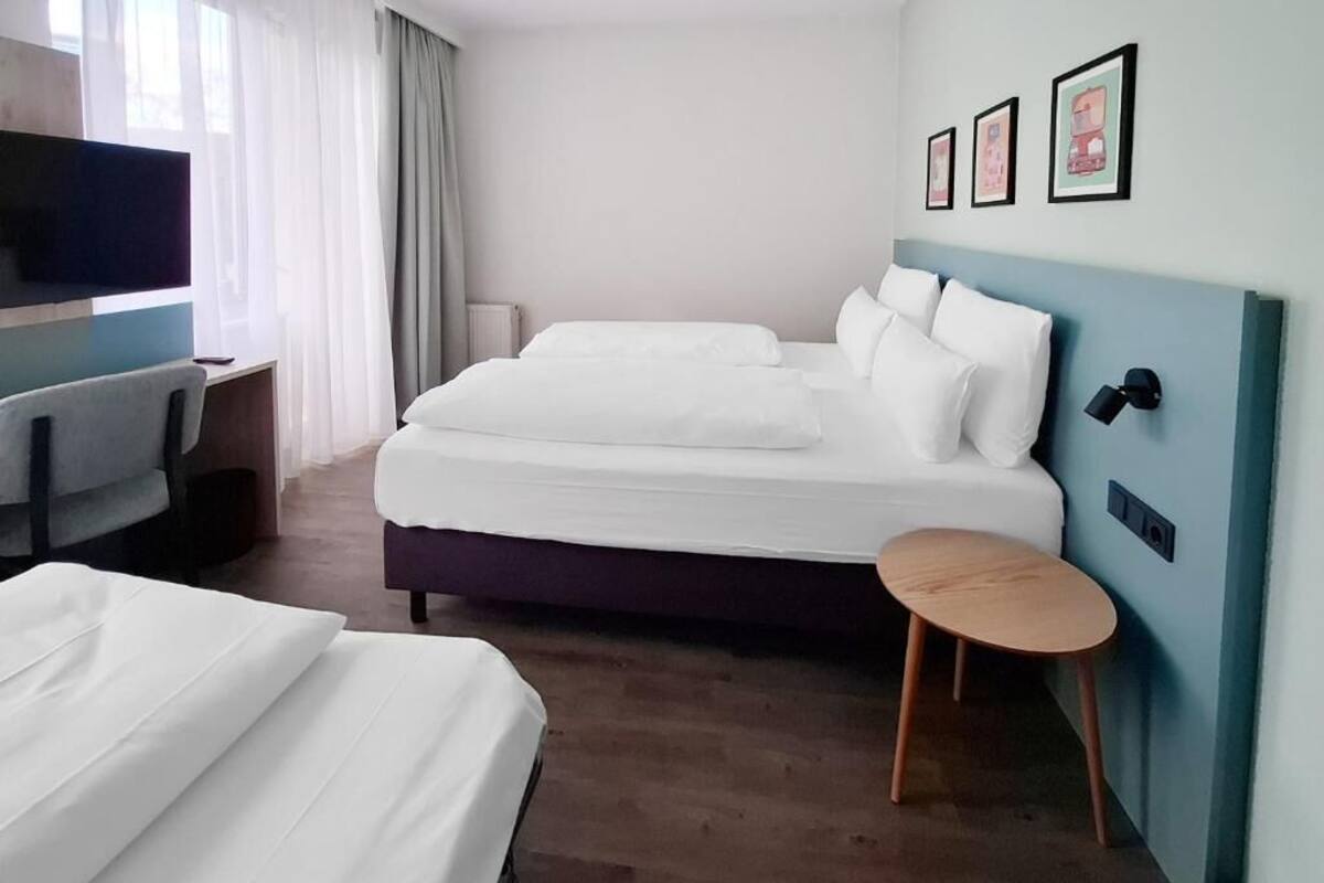 A hotel room with a bed, a desk, a chair, a TV, and a small table.