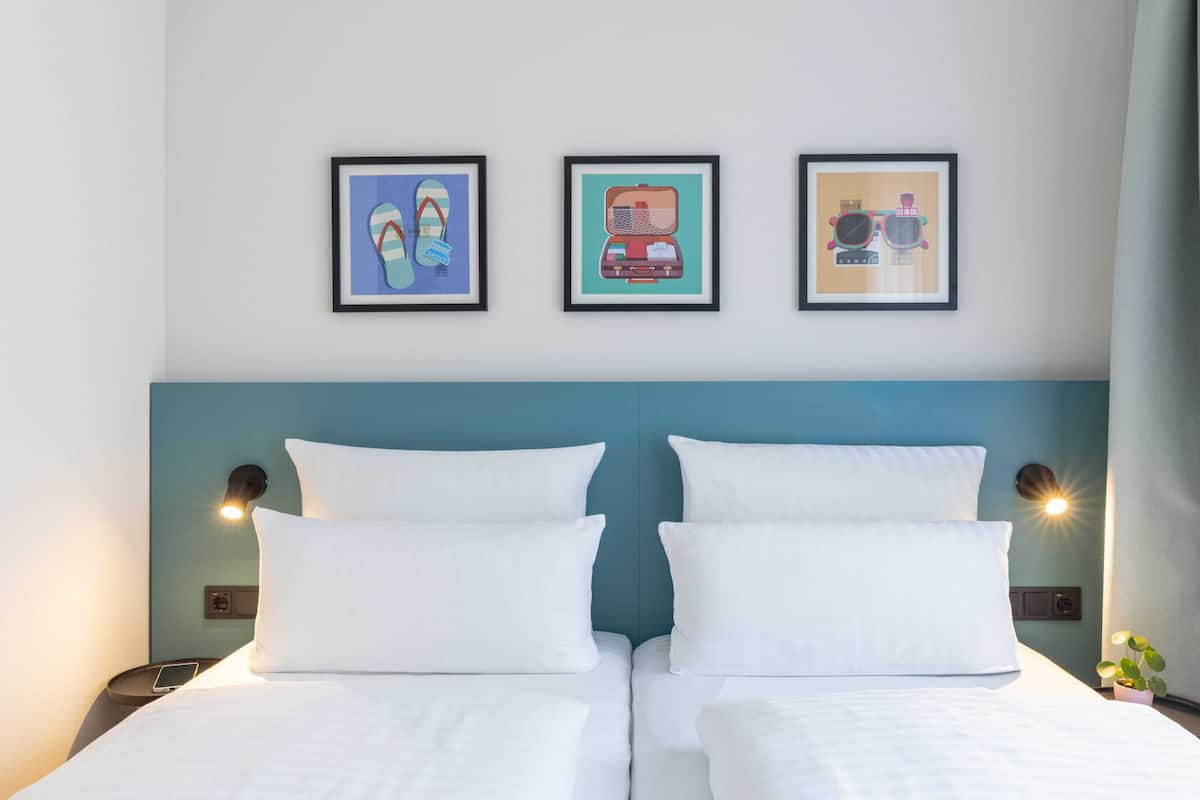 Ein Doppelbett mit weißen Bettwäsche, ein türkisblaues Kopfteil und drei gerahmte Kunstwerke an der Wand.