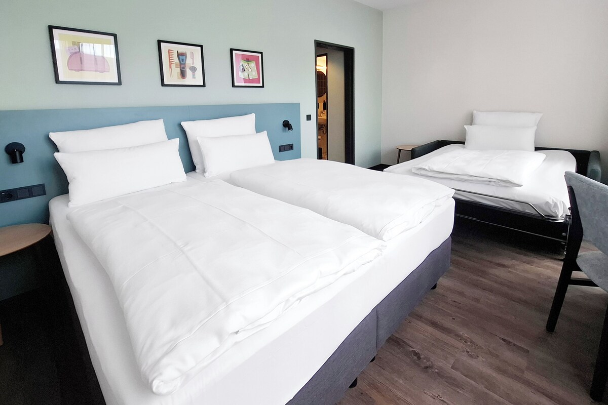 A hotel room with two beds, a blue accent wall, and framed artwork.