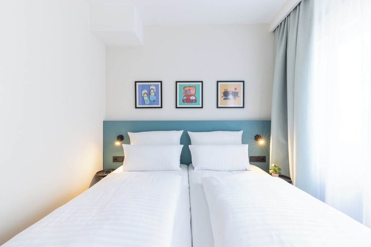 A hotel room with a bed, two bedside tables, a headboard, and three framed pictures on the wall.