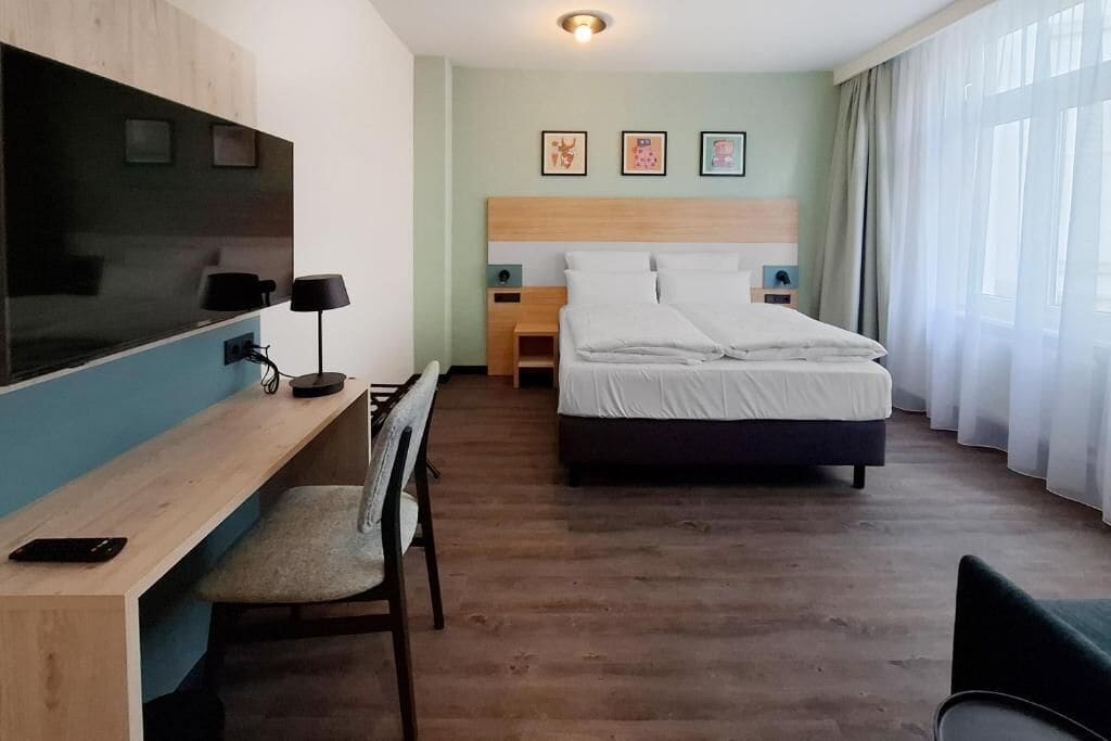 A hotel room with a bed, desk, chair, and a TV.